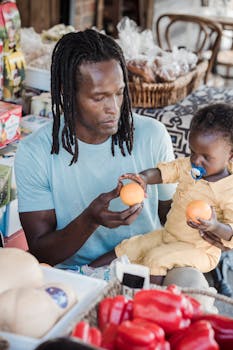 A father and his young child sharing fresh oranges at an outdoor market.