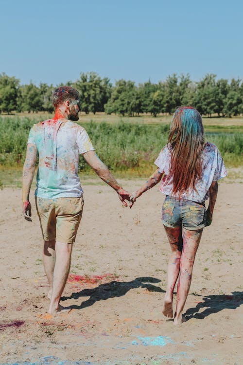 A Couple Walking Holding Hands on the Dirt Near the Grass Field