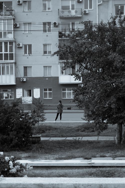 Free Monochrome view of an apartment facade with a person walking on a sidewalk. Stock Photo