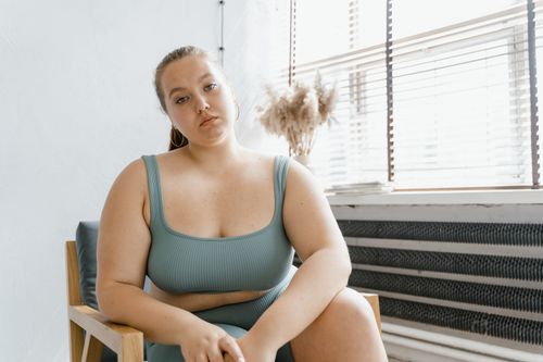 Free A plus size woman in activewear, sitting confidently in a chair indoors, looking at the camera. Stock Photo