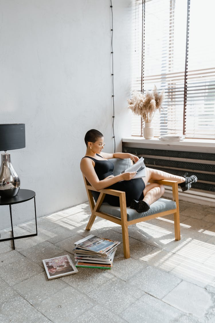 A Woman Reading A Book While Sitting On A Chair