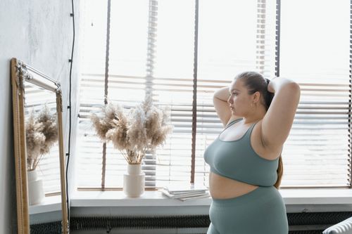 Free A plus-size woman in activewear admires her reflection indoors, promoting body positivity and self-esteem. Stock Photo