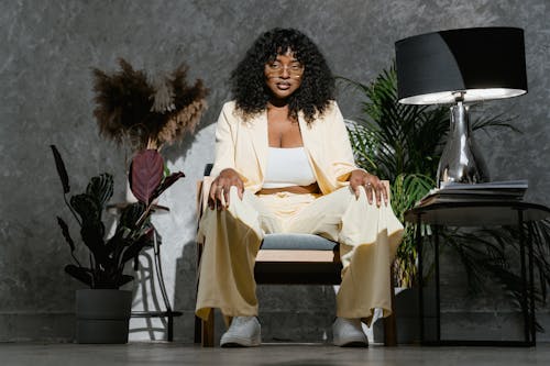 A Woman in Yellow Suit Siting on a Chair Near a Lampshade and Plants