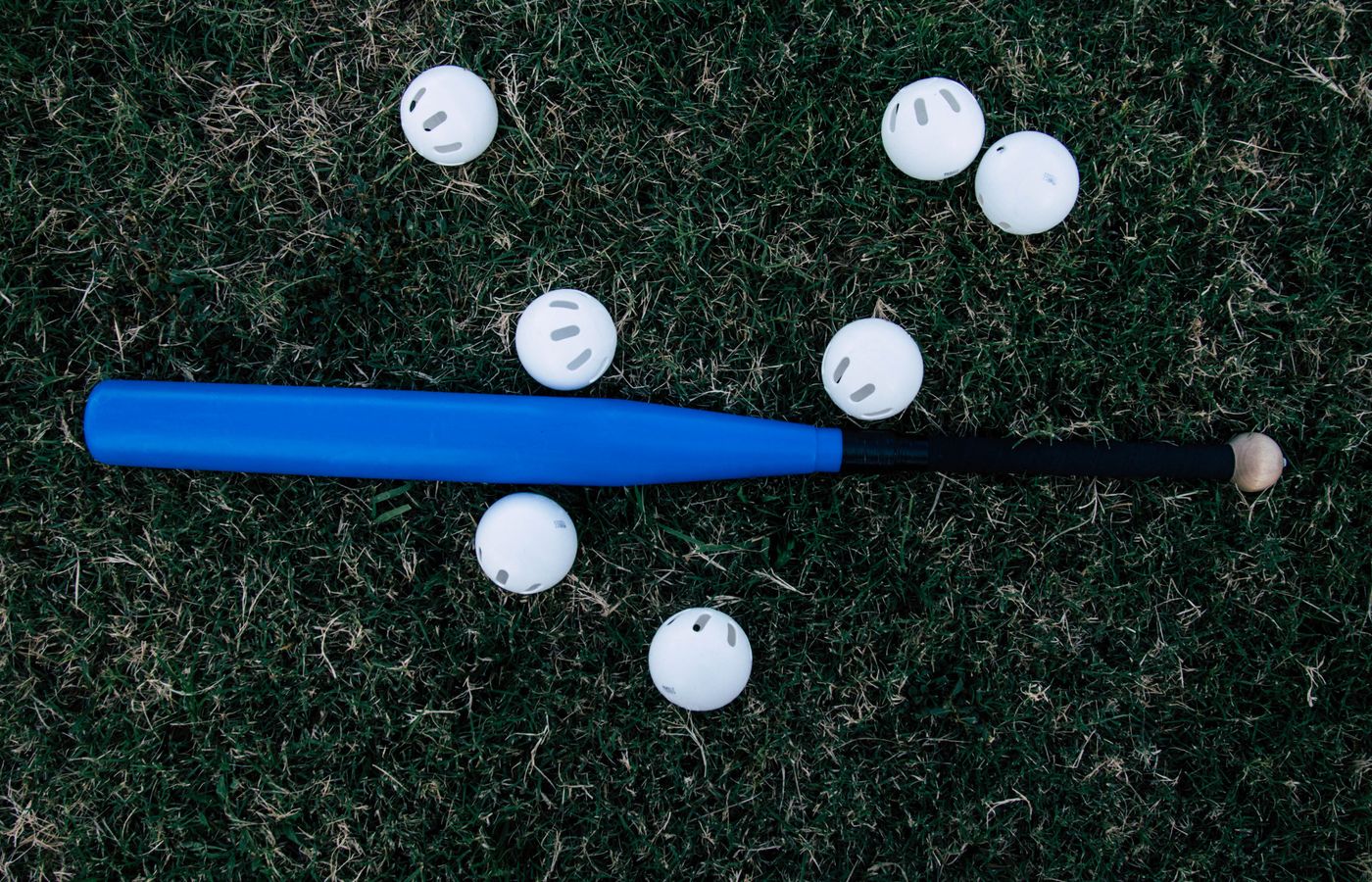 A blue baseball bat surrounded by white practice balls lying on green grass outdoors.