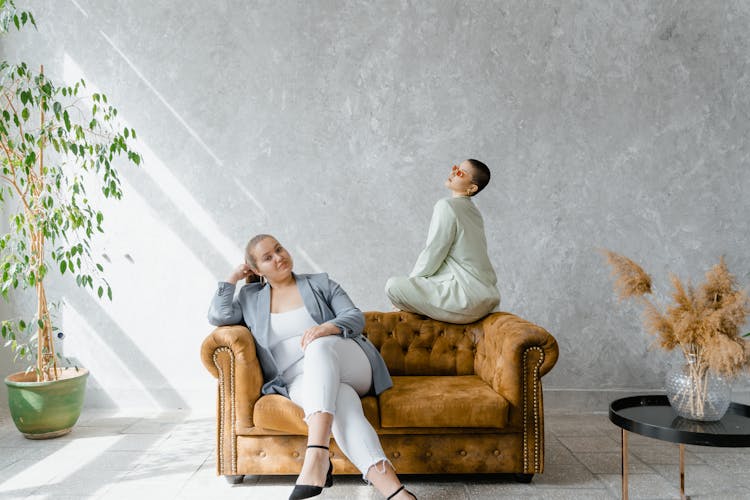 Two Women Sitting On Brown Couch