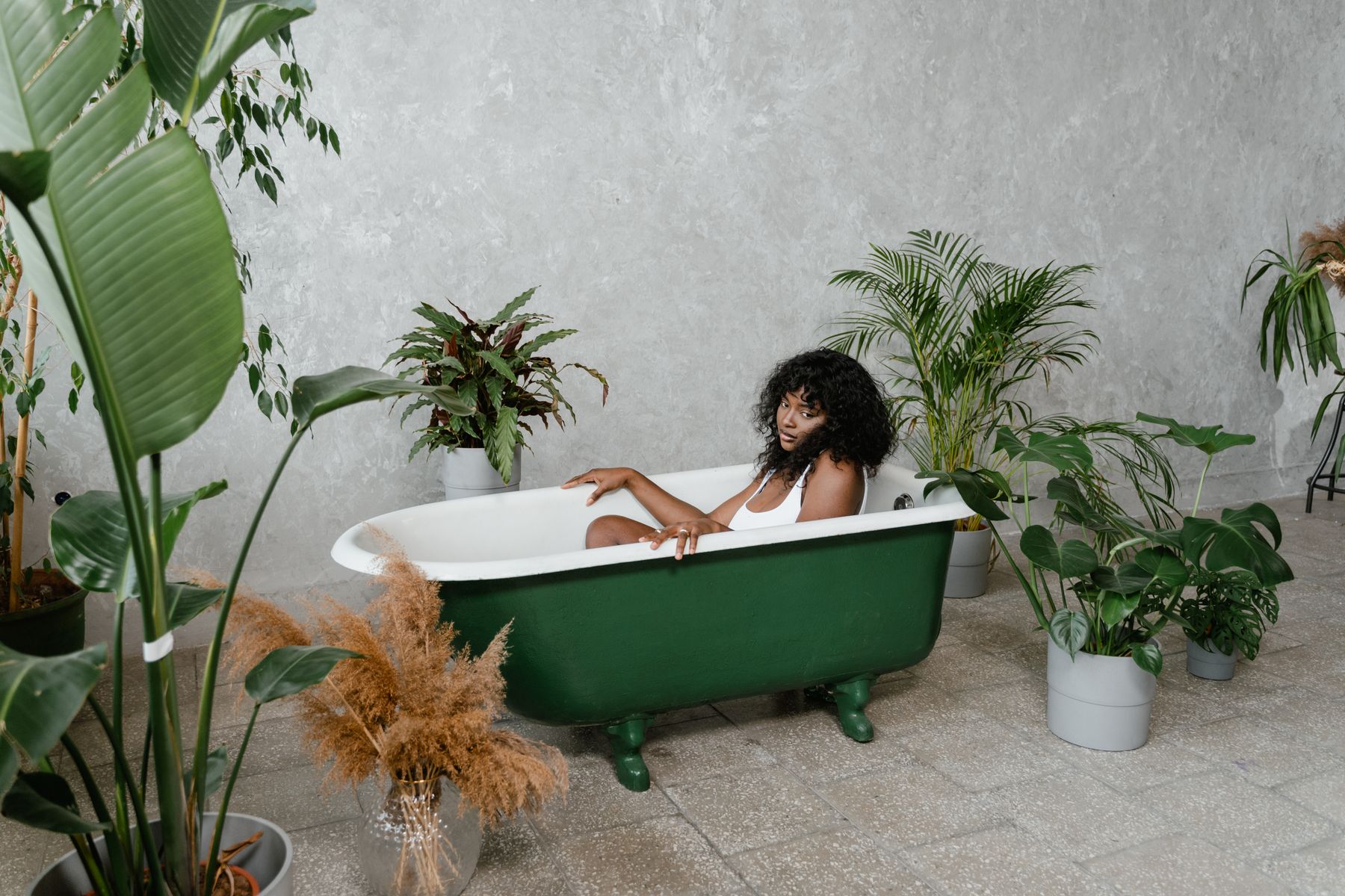 Green bathtub surrounded by lush plants in a bright boho-style bathroom