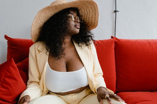 Confident plus size woman in fashionable attire lounging on a red sofa indoors.