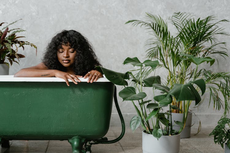 A Curly Haired Woman In A Green Bathtub Near Potted Plants