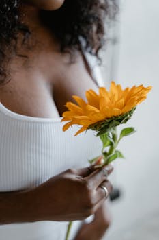 A close-up of a woman holding a bright yellow sunflower, symbolizing beauty and positivity.