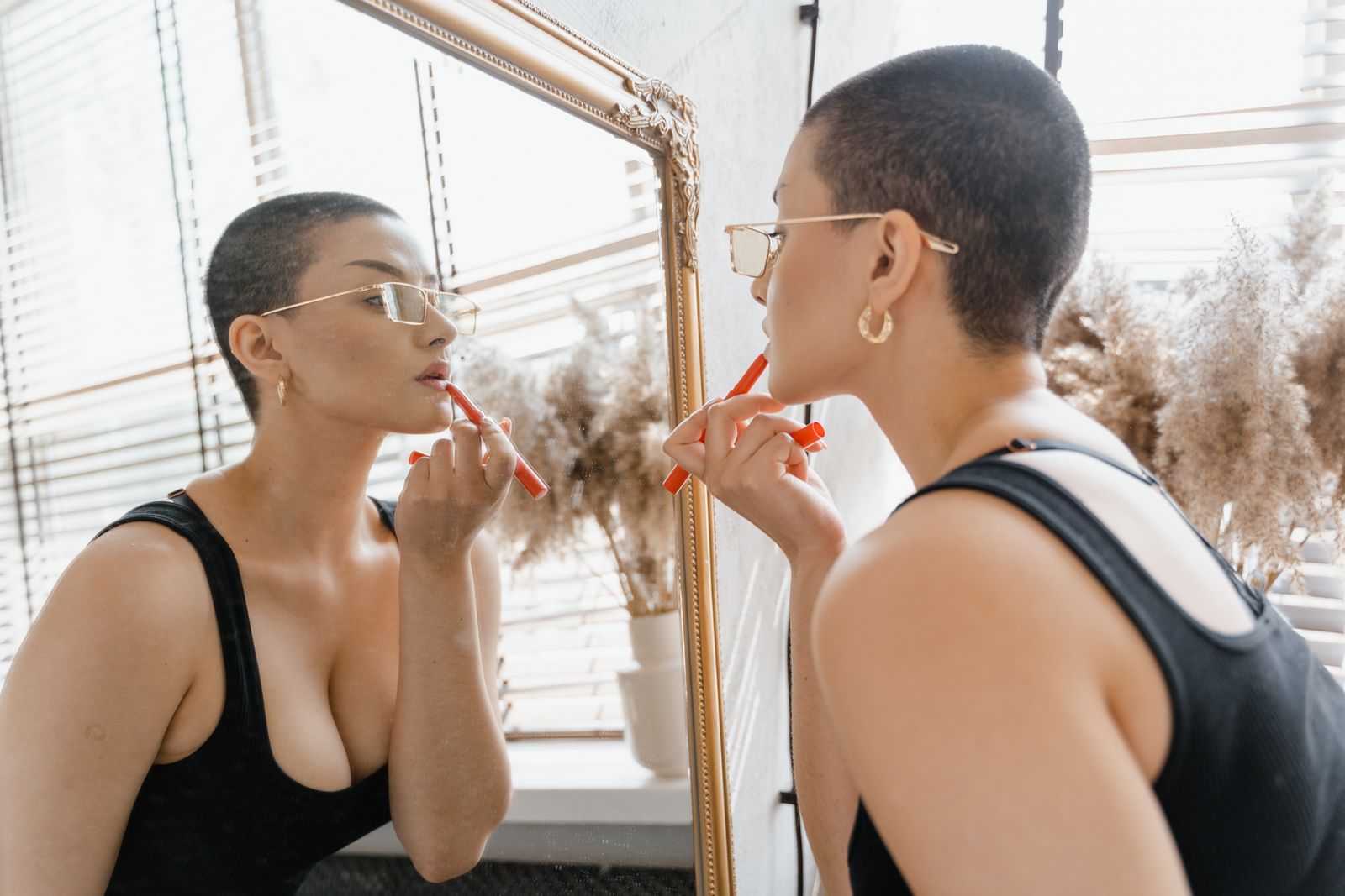 A woman in glasses applies lipstick while looking in the mirror. Bright, modern, and stylish.