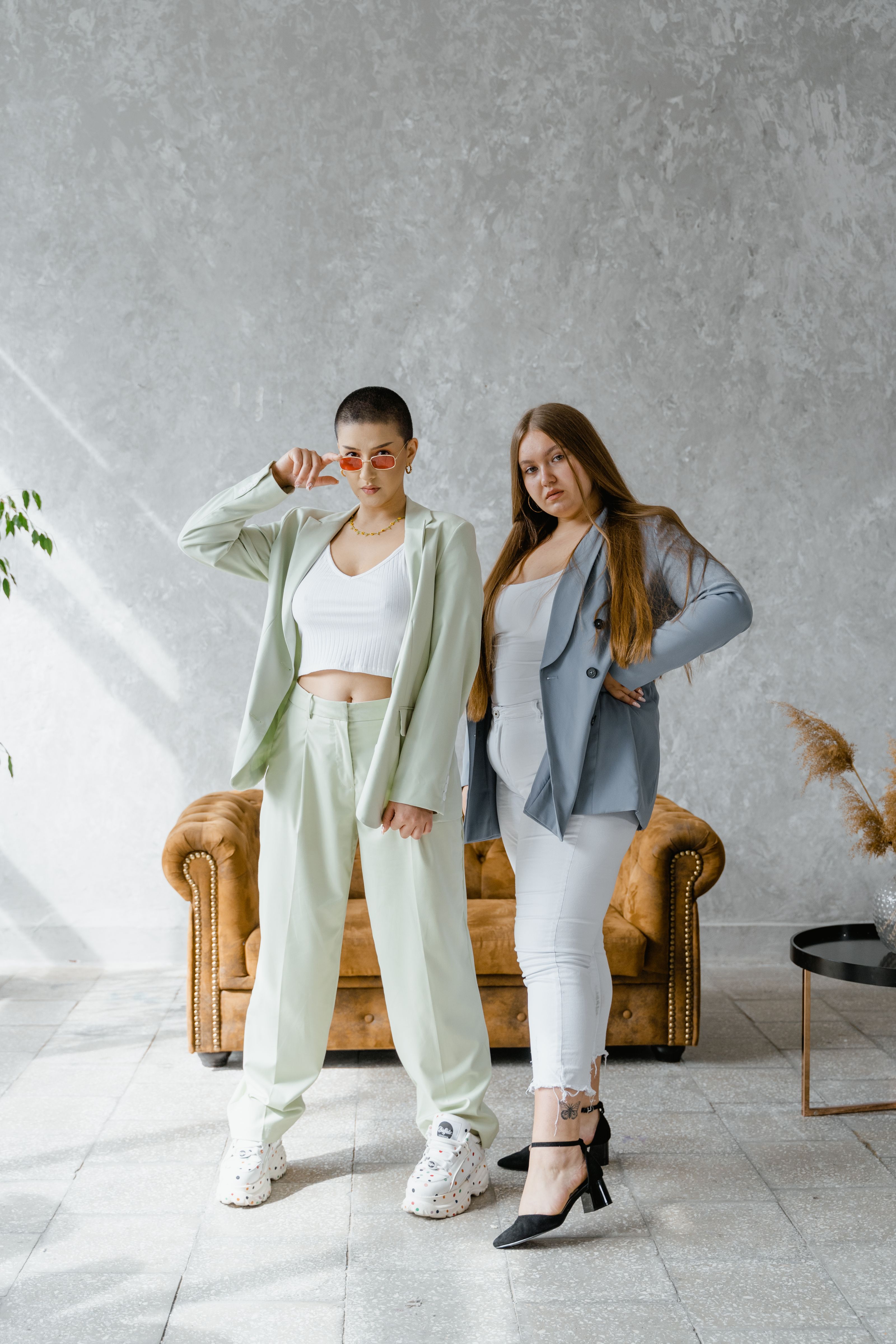 Duas mulheres em roupas estilosas posando com confiança em um ambiente interno moderno.