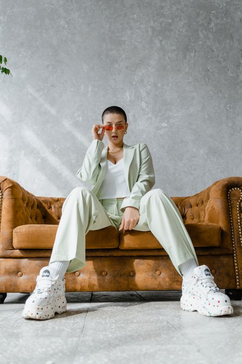 Free Trendy woman wearing a mint suit and sneakers, sitting confidently on a vintage couch indoors. Stock Photo