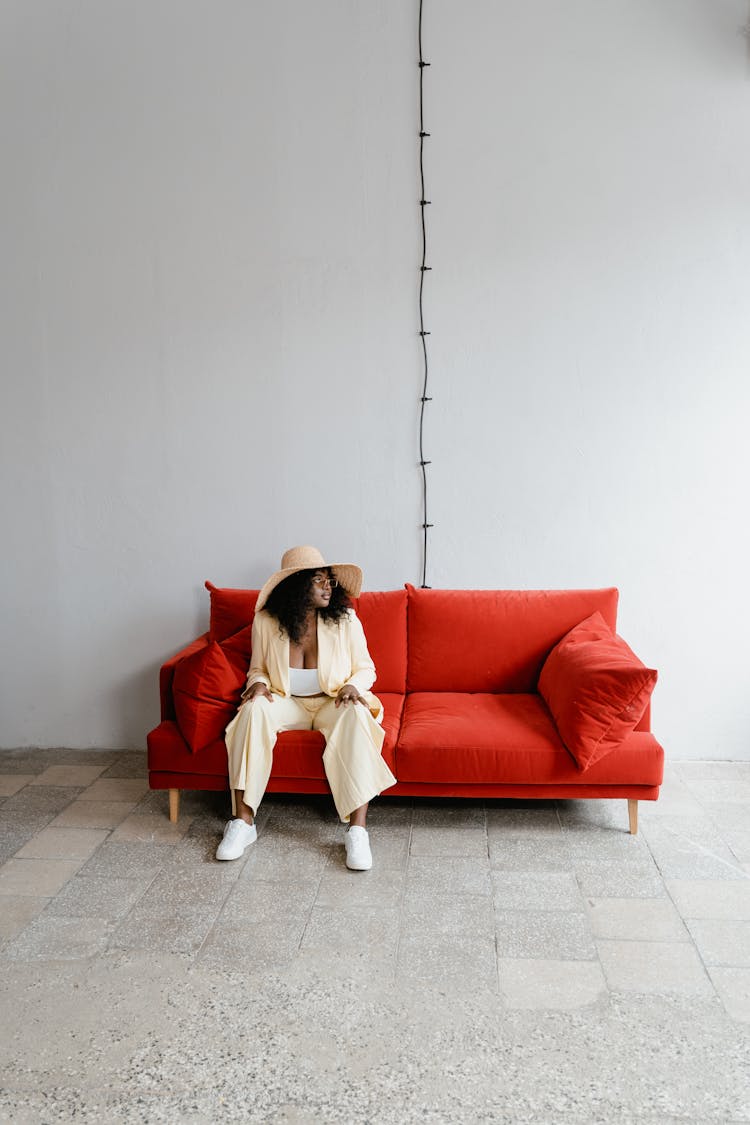 Woman In Hat Sitting On Red Sofa 