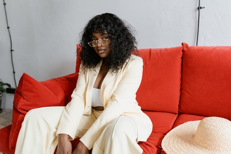 A Woman In A Stylish White Outfit Sitting On A Red Couch