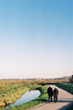 An elderly couple strolls down a countryside road on a clear day.