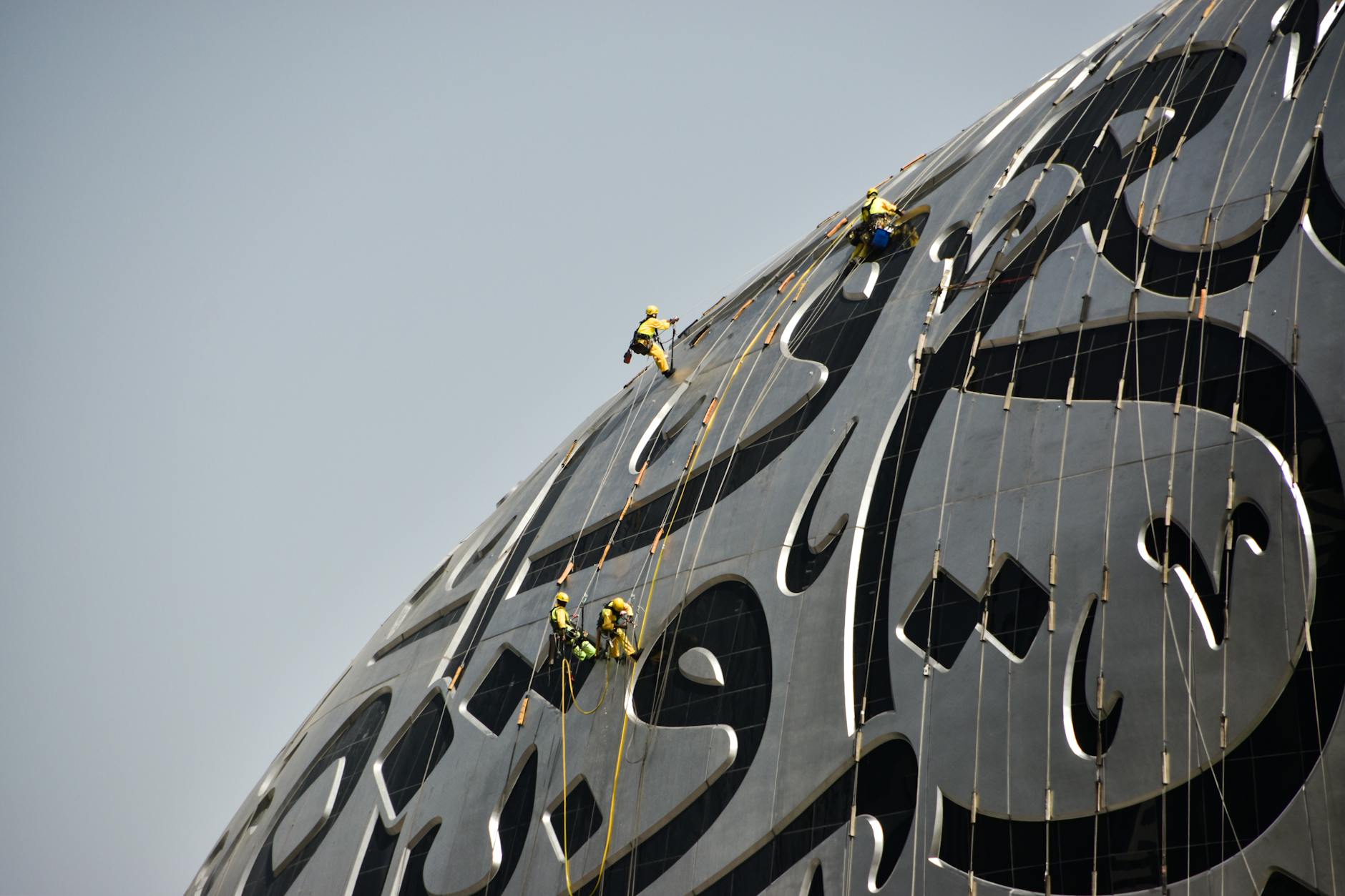 Construction workers climb a modern building with Arabic script in Dubai.