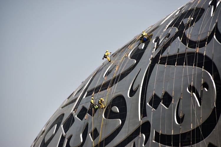 Architectural Detail With Arabic Script And Construction Workers On Ropes