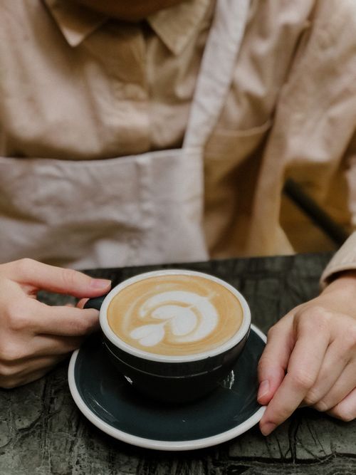 Free Crop anonymous barista in uniform sitting at table with cup of aromatic coffee in cafe Stock Photo