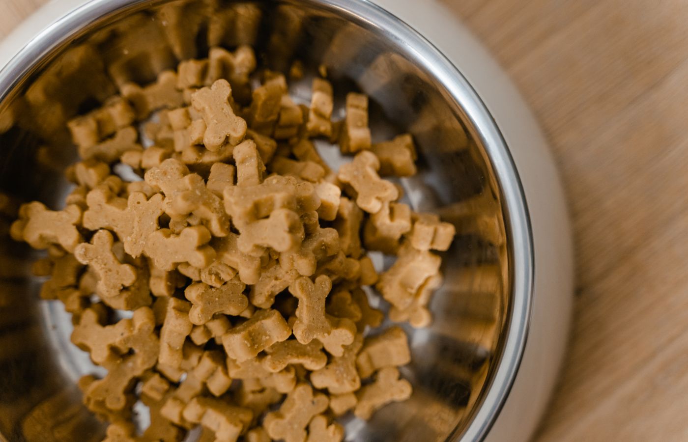 A close-up view of dog bone-shaped biscuits in a stainless steel bowl on a wooden surface.