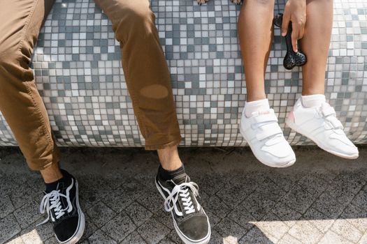 Close-up of two people wearing sneakers sitting on a mosaic bench outdoors.
