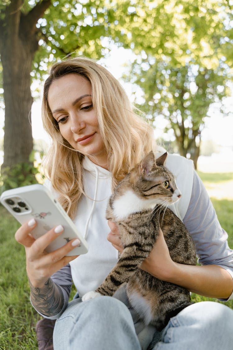 A Woman Using Her Phone While Holding Her Cat