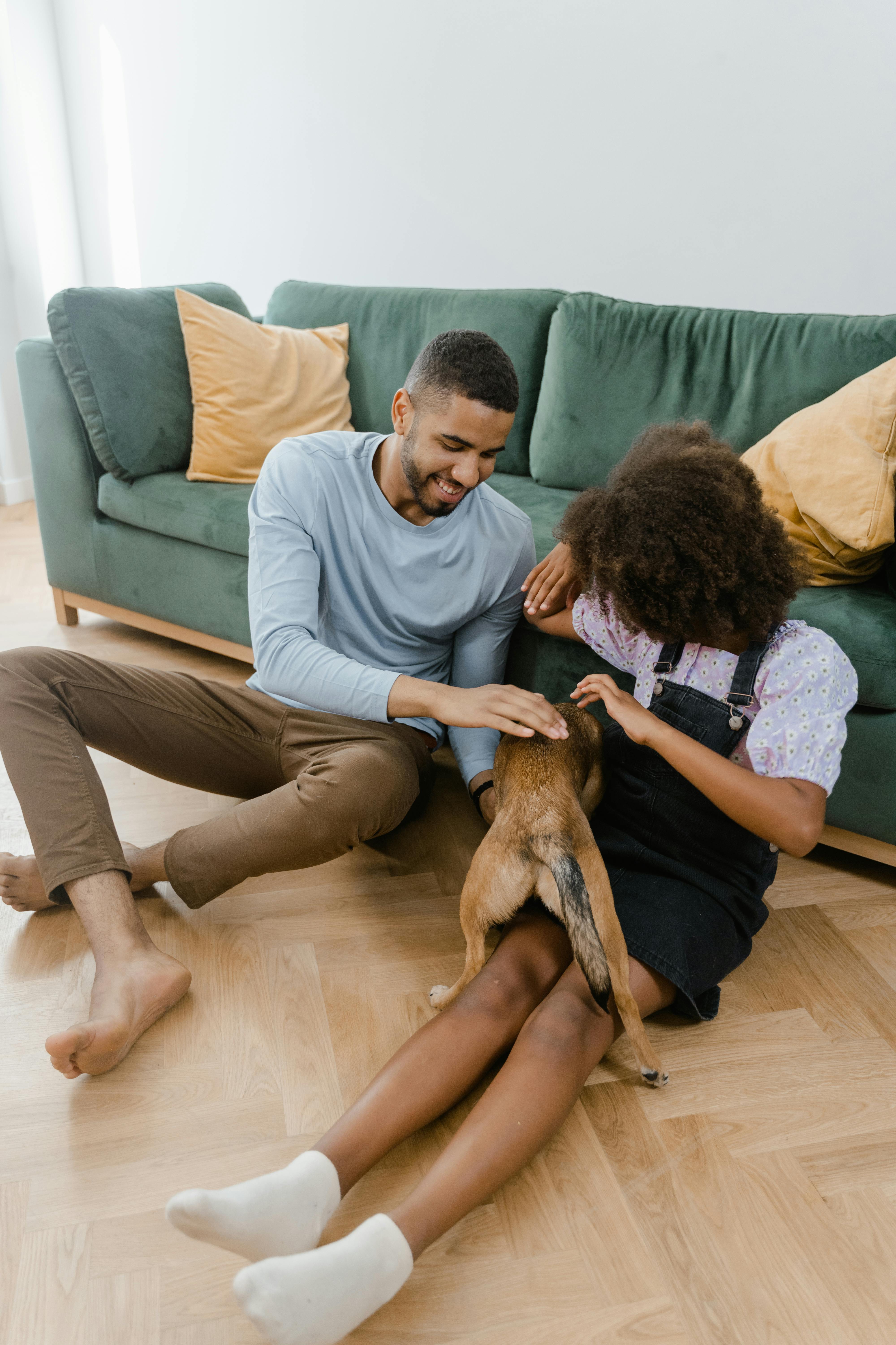 man and girl sitting on the floor playing with a dog