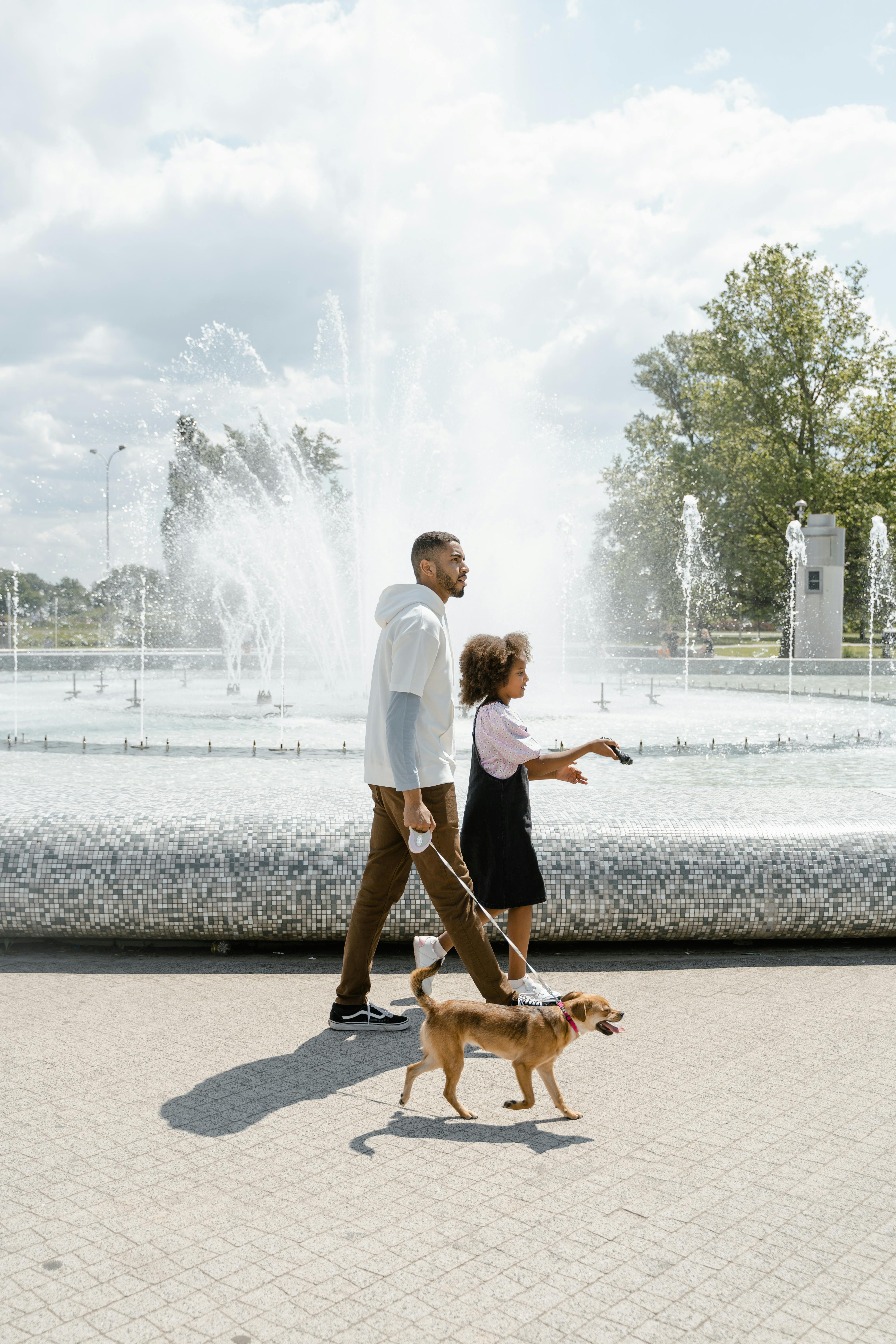 a man walking at the park with his daughter and his dog