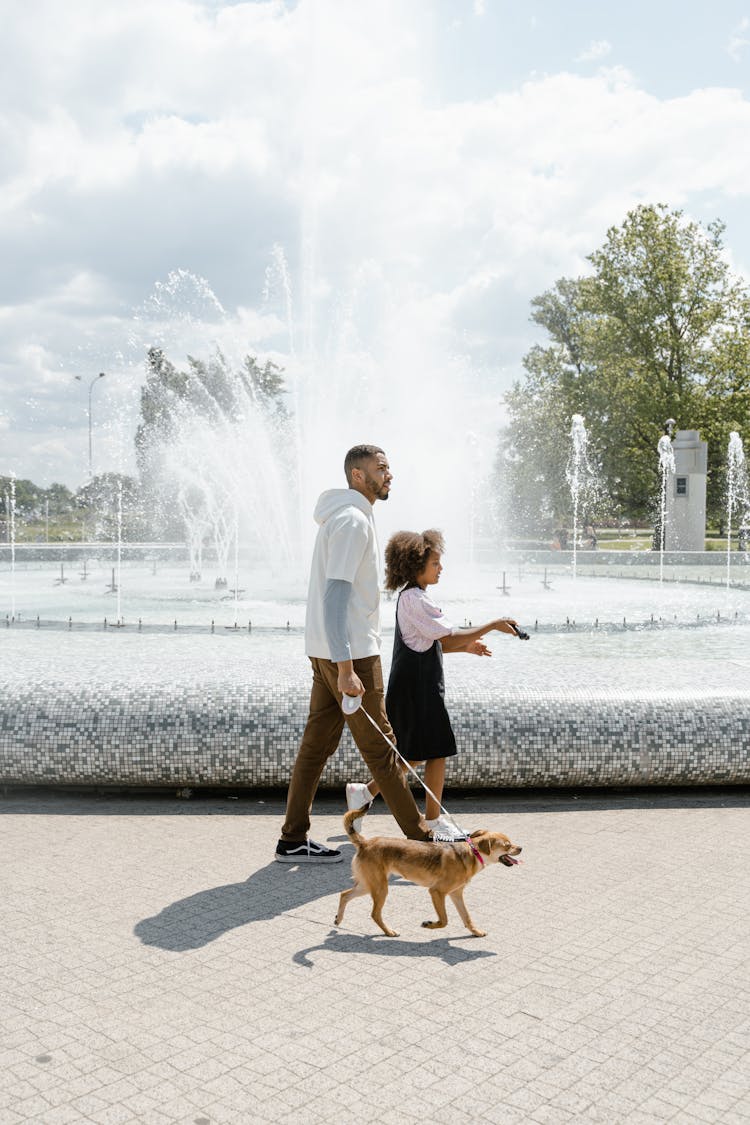 A Man Walking At The Park With His Daughter And His Dog