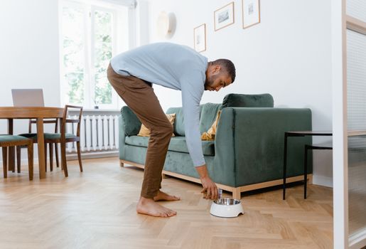 A man places a dog bowl on the floor in a modern living room with green furniture.
