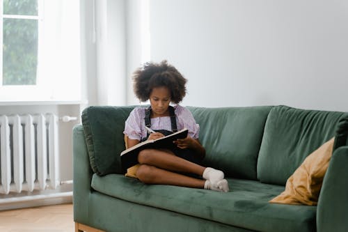 Free A Woman Sitting on a Couch while Writing on a Notebook Stock Photo