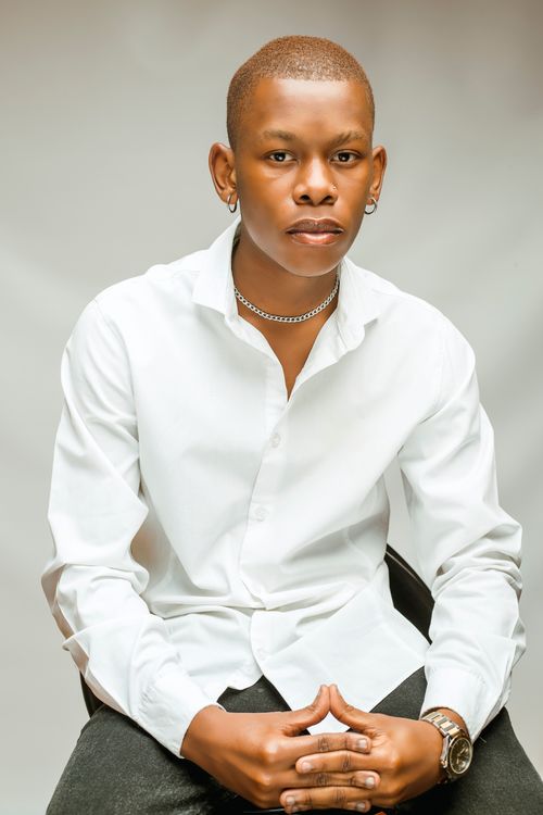 Free Studio portrait of a young man dressed elegantly in a white shirt, seated against a gray backdrop. Stock Photo