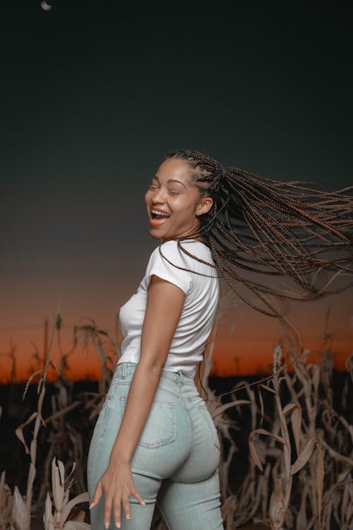 Smiling Woman in White Shirt and Denim Pants Standing in a Field During Sunset 