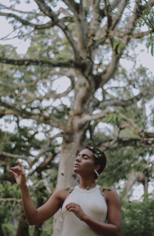 Free A peaceful woman poses outdoors with lush green trees in the background, embodying tranquility and connection with nature. Stock Photo