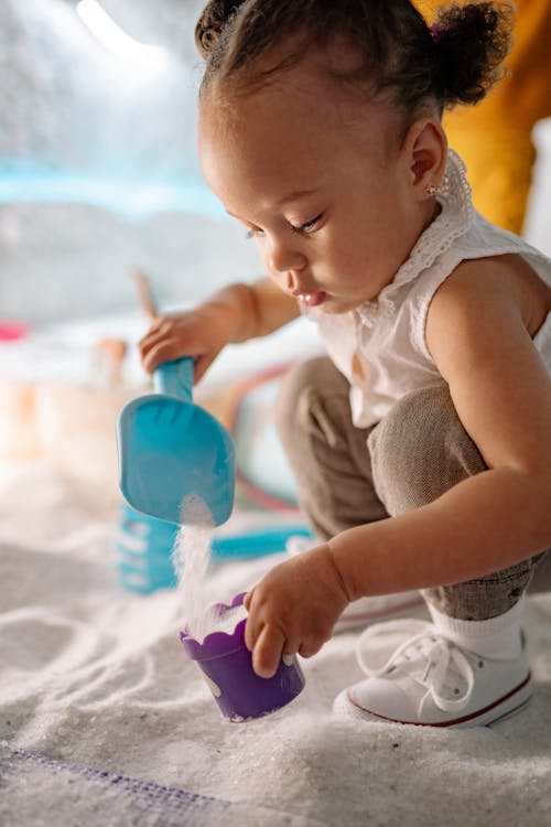 A Girl in White Tank Top Shoveling Sugar into a Plastic Container