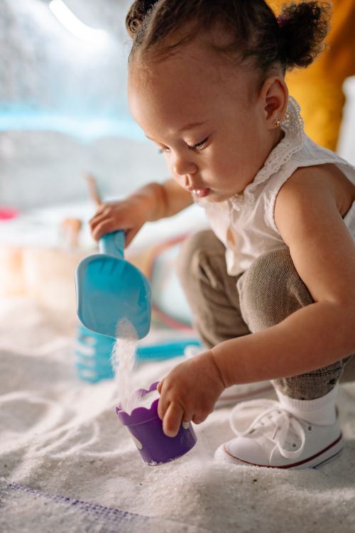 Free A cute toddler focused on playing with sand using a toy shovel indoors, highlighting fun and playtime. Stock Photo