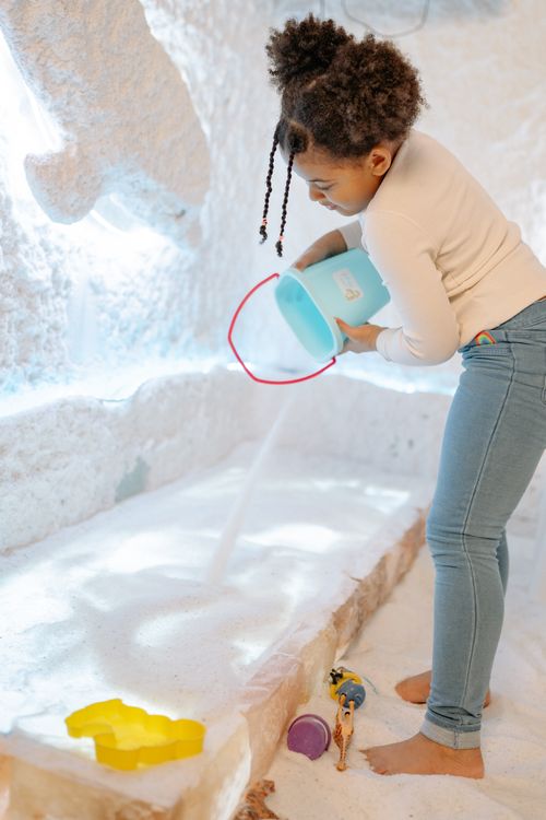 Free Child pouring sand from bucket in a bright indoor play area, engaged in creative play. Stock Photo