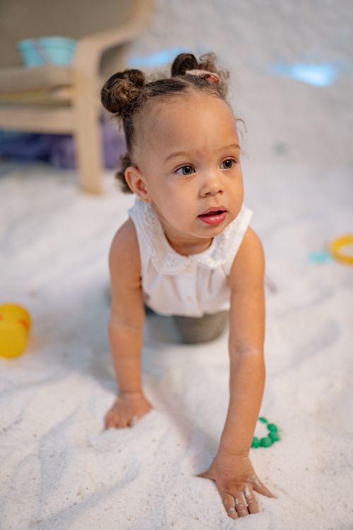 Free A young child crawling happily on a soft play area indoors, surrounded by toys. Stock Photo