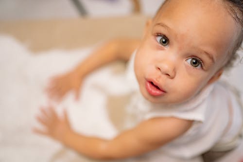 Baby in White Tank Top Lying on White Textile