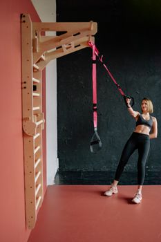 Woman exercising with suspension trainer indoors. Fitness workout for strength and flexibility.