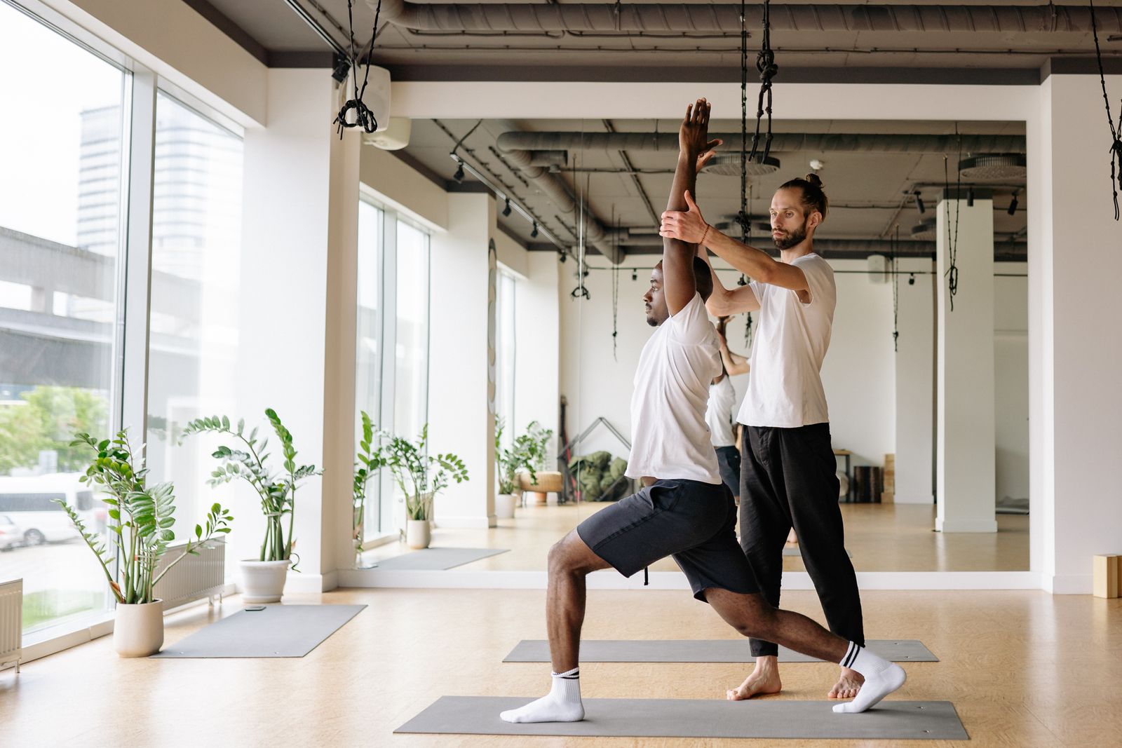 Yoga instructor guiding a student through pose alignment in a bright studio