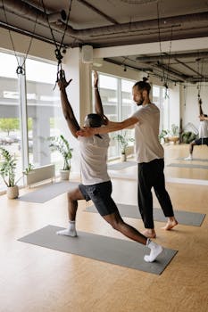 Instructor helps student with yoga pose in bright studio, promoting wellness and fitness.