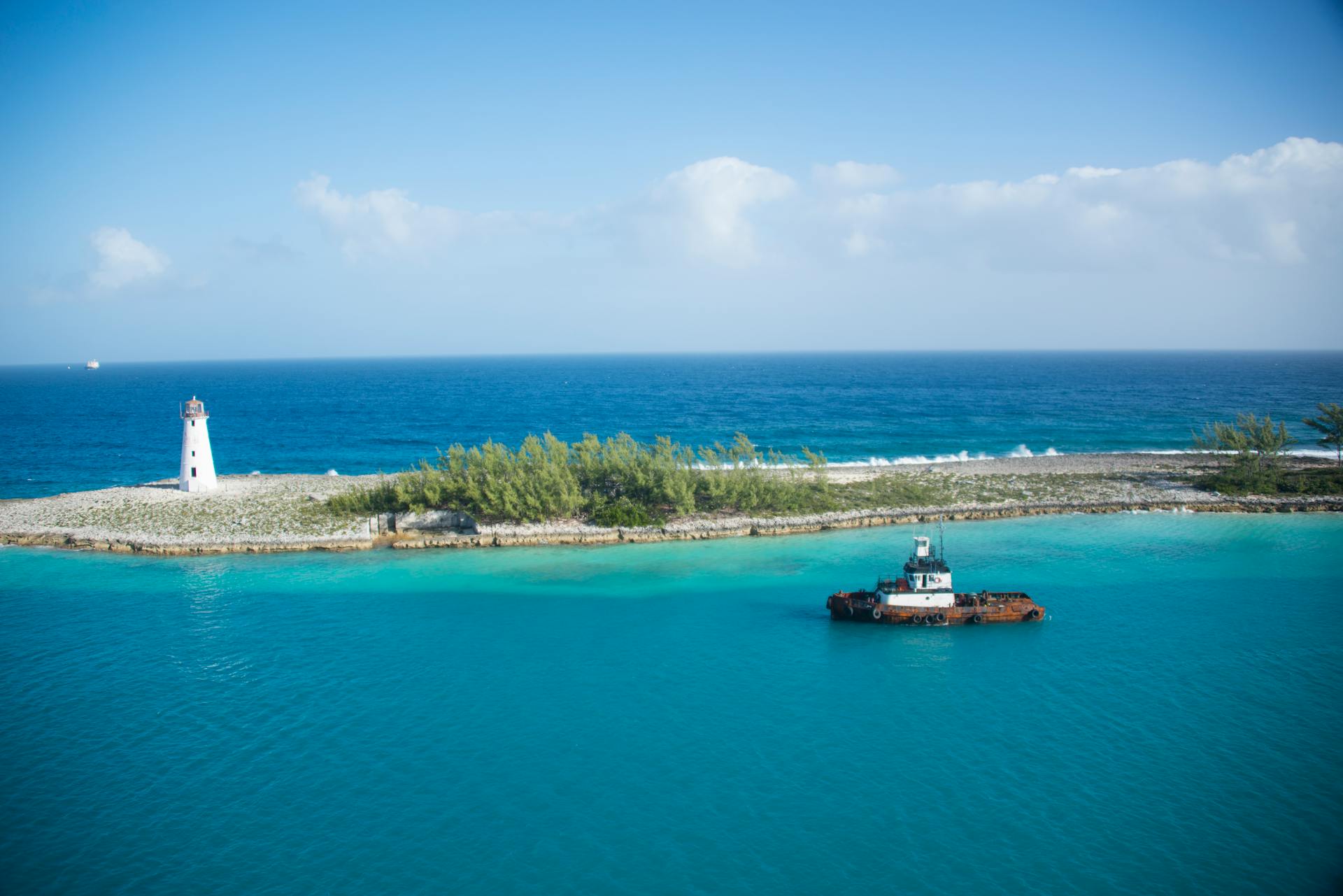 Scenic view of a tranquil island landscape featuring a lighthouse and a lone tugboat on a clear day.