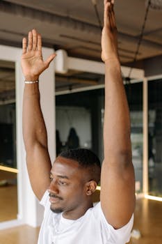 Confident man raising arms during stretching exercise at a modern gym.