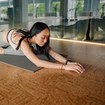Young woman in yoga wear practicing a stretch on a mat indoors.