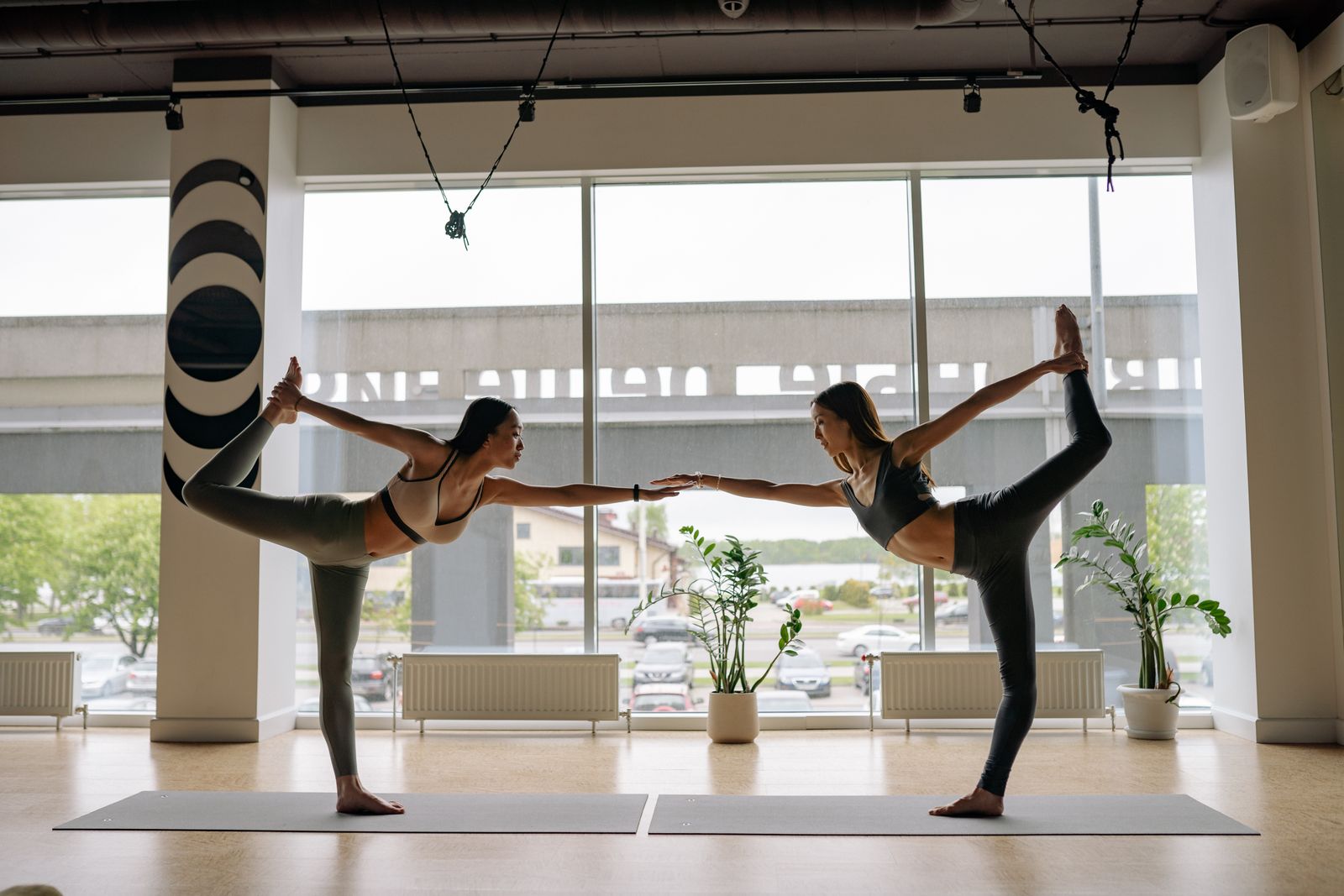 Two women practicing a balanced partner yoga pose together in a bright modern studio