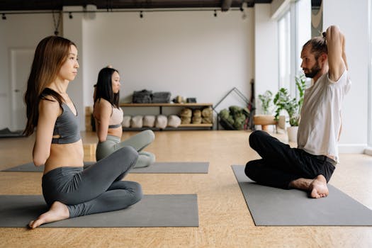 A mixed-gender group practicing yoga indoors, focusing on meditation and stretching.