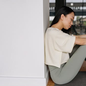 Side view of a young woman in yoga attire relaxing indoors, sitting against a wall.
