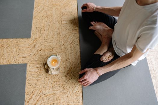 Adult meditating in lotus pose on yoga mat with candle, creating a calming atmosphere.