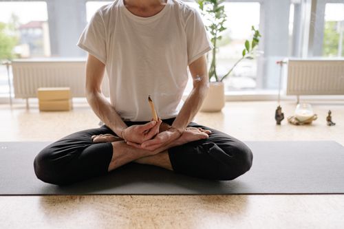 Free A man sits cross-legged holding an incense stick during yoga meditation indoors. Stock Photo