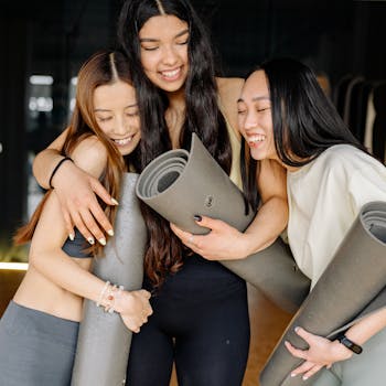 Three young women joyfully hugging and holding yoga mats, symbolizing friendship and healthy living.